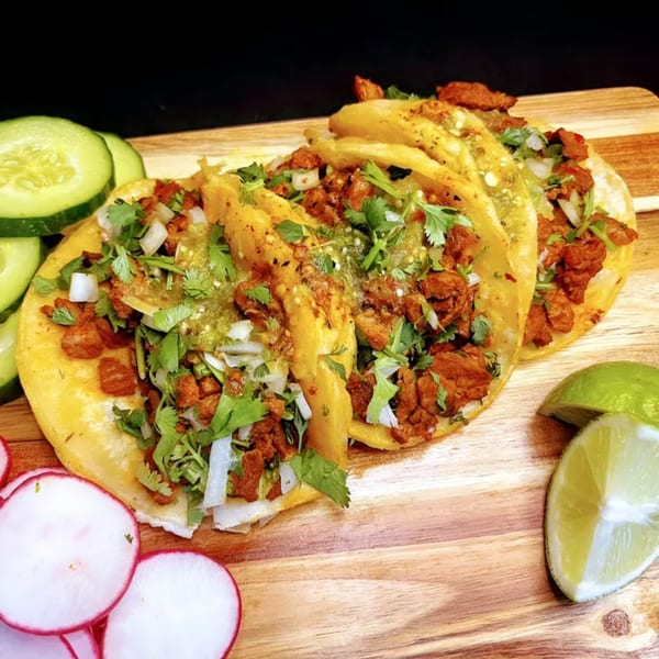 Three Takozz tacos with meat, cilantro, and salsa verde, alongside sliced cucumbers, radishes, and limes.