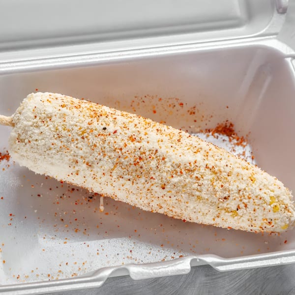 Elote, Mexican street corn, coated in white cheese and chili powder in a takeout container.
