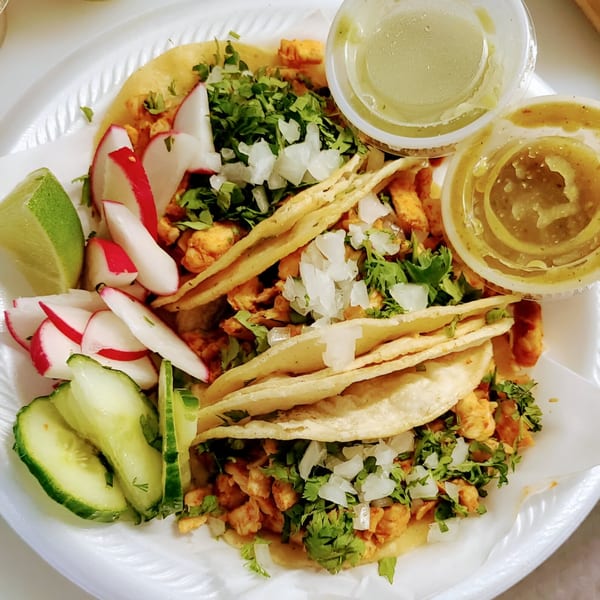 Three Takozz chicken tacos with cilantro, onions, radishes, cucumbers, lime, and two sauces.