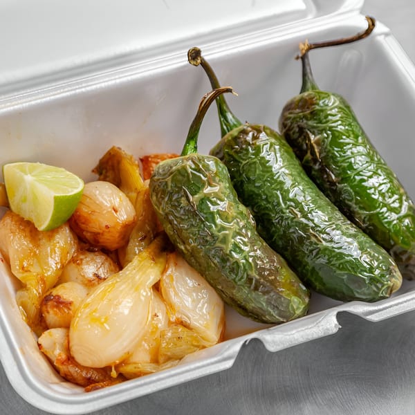 Takozz Mexican side dish with grilled green peppers, caramelized onions, and a lime wedge in a takeout container.